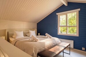 A bedroom with a sloped ceiling, a large bed with a headboard, a bench, and a window with a view of trees. - Stay North - Apple House (Kangasala)