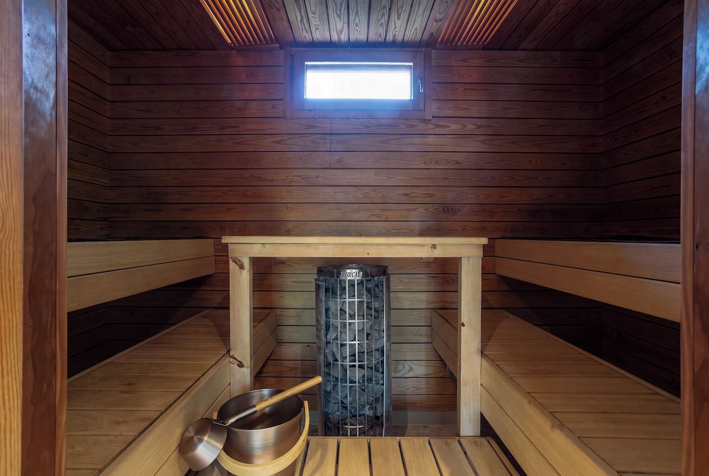 A sauna room with wooden walls, a bench, a sauna heater, and a skylight.