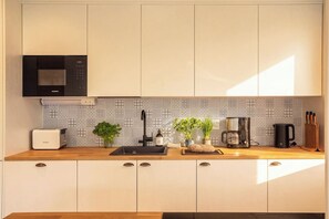 A modern kitchen with a Siemens microwave, a Bosch toaster, a sink with a faucet, a coffee maker, and a knife block. - Stay North - Apple House (Kangasala)