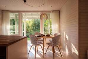 A dining area with a wooden table and checkered chairs, large windows with curtains, and a hanging light fixture. - Stay North - Apple House (Kangasala)