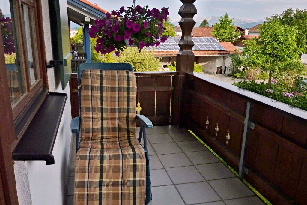A balcony with a plaid chair, a hanging flower basket, and a view of houses and trees.