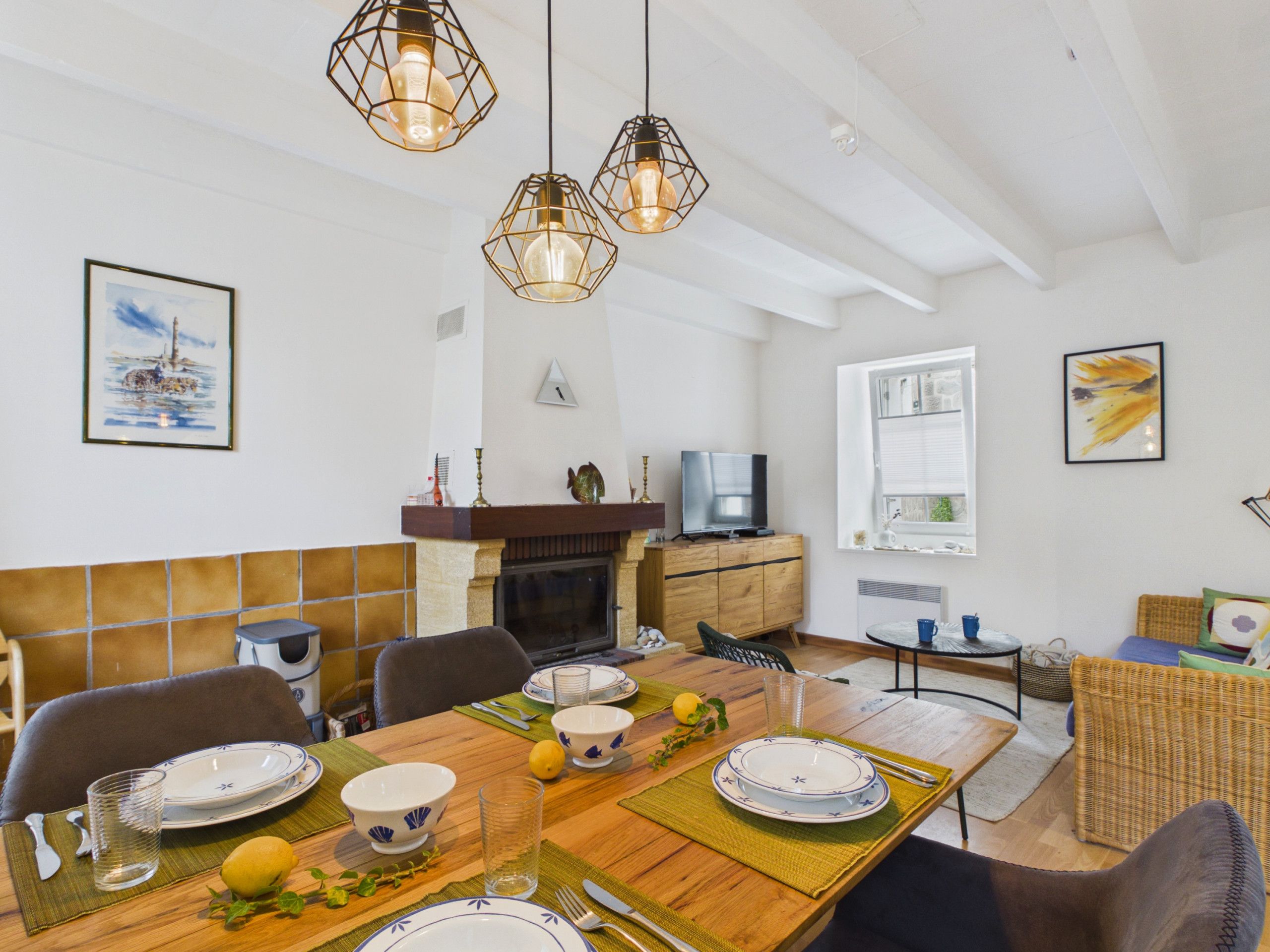 A dining area with a wooden table set for four, a fireplace, and a television in the background.
