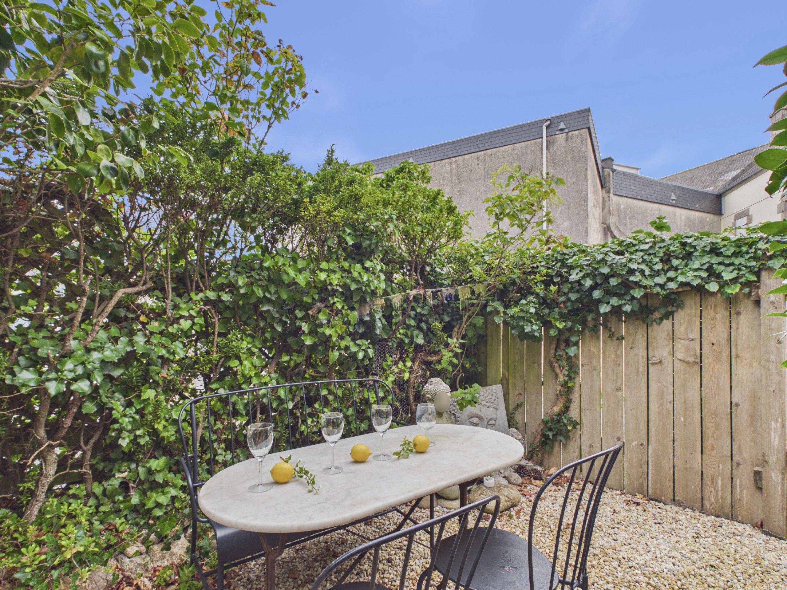 An outdoor dining area with a round table, four chairs, and a wooden fence covered in greenery.