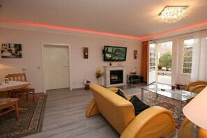 A living room with a fireplace, a television, and a dining area with a table and chairs. - Seesternchen - Residence under the Linden trees (Kühlungsborn)