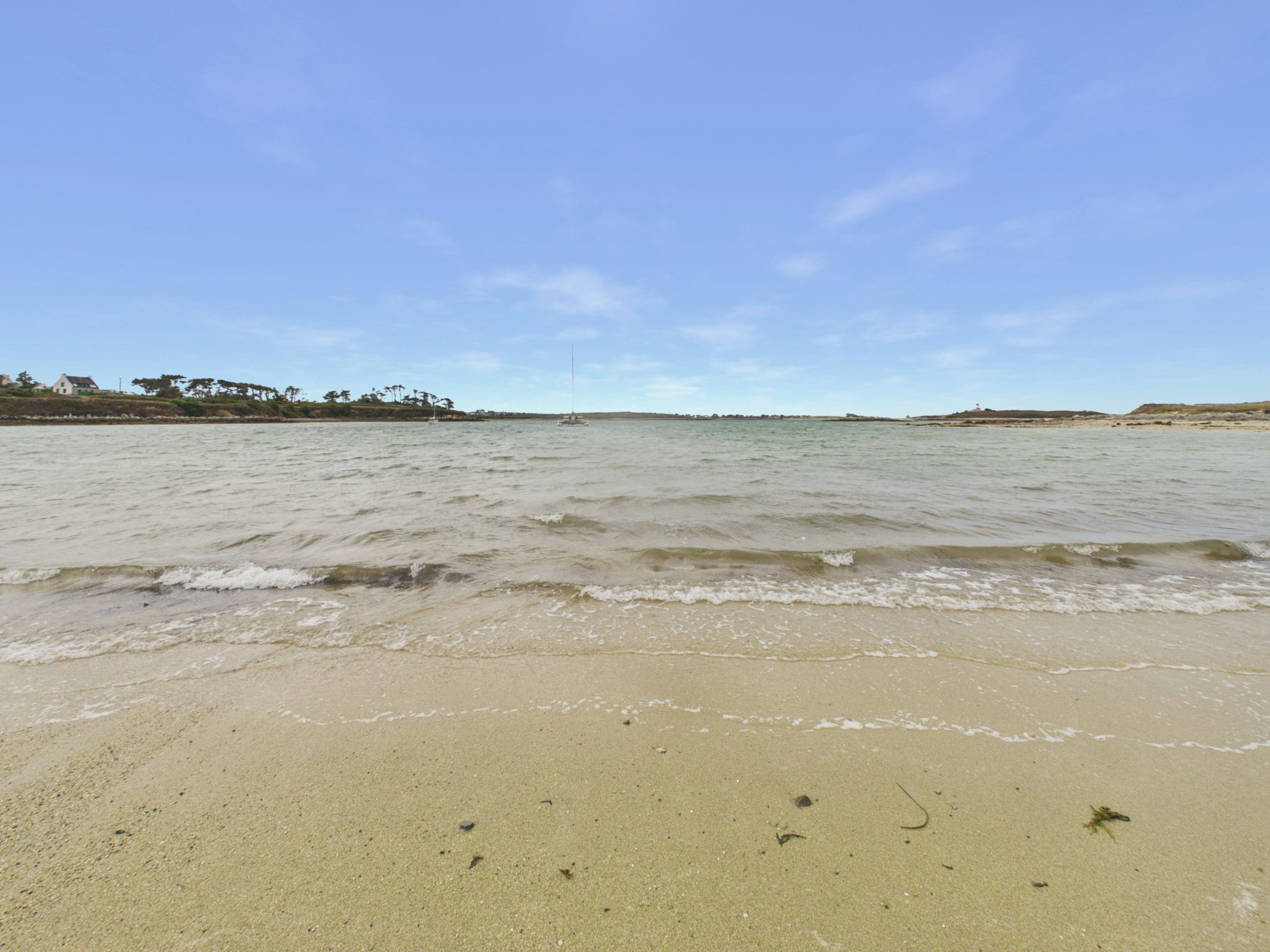 A beach with gentle waves, a clear sky, and distant land with vegetation.