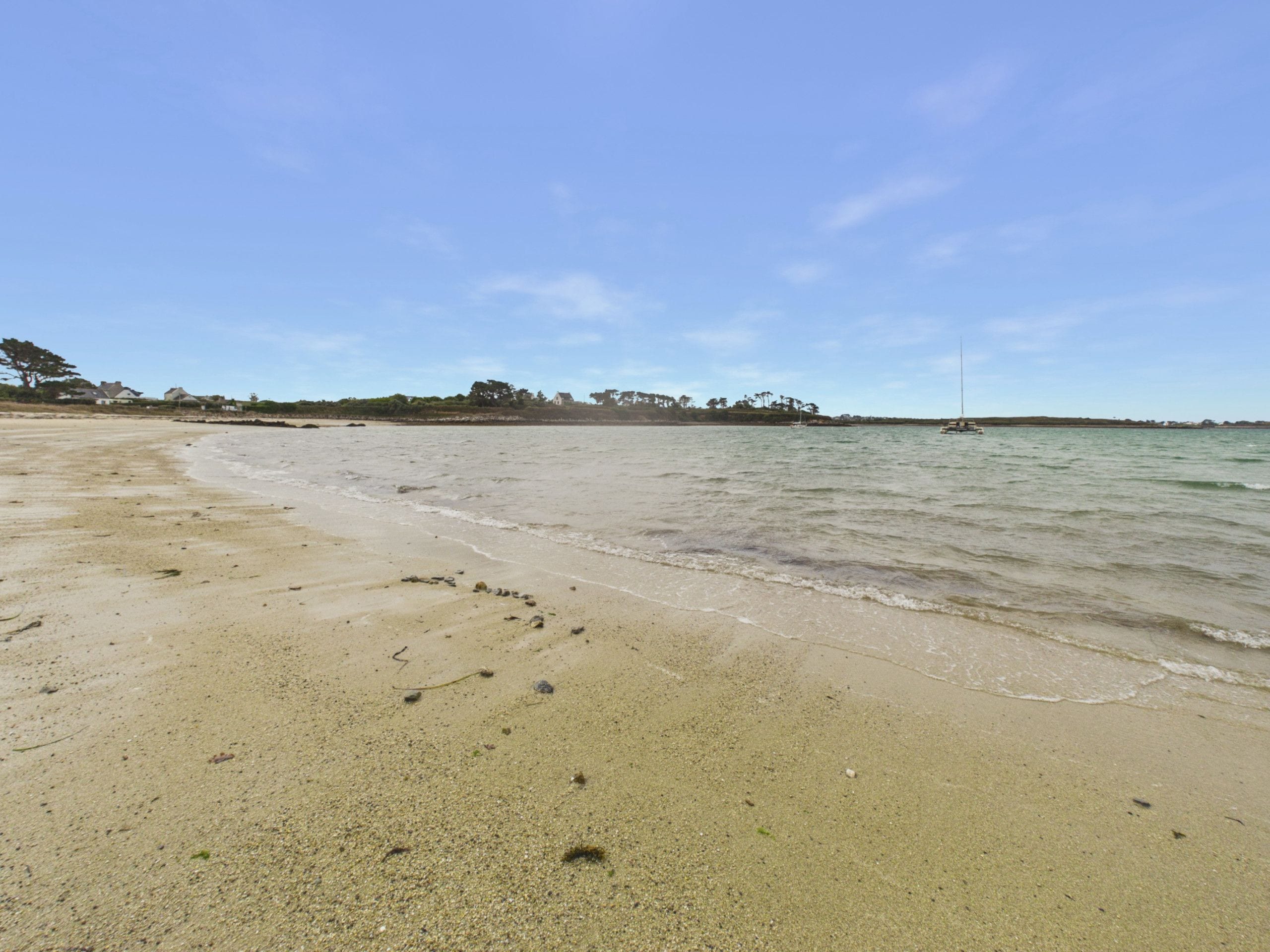 A beach with a clear sky, calm water, and footprints in the sand.