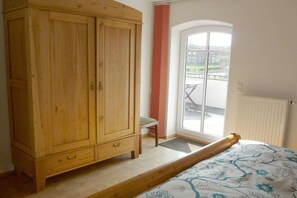 A room with a wooden wardrobe, a single bed with a floral bedspread, a chair, and a window with a view of the outside. - Country house at Grashof (Offenbüttel)
