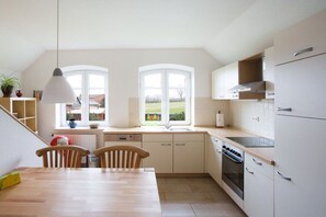A kitchen with a dining table, chairs, a stove, and a window. - Country house at Grashof (Offenbüttel)