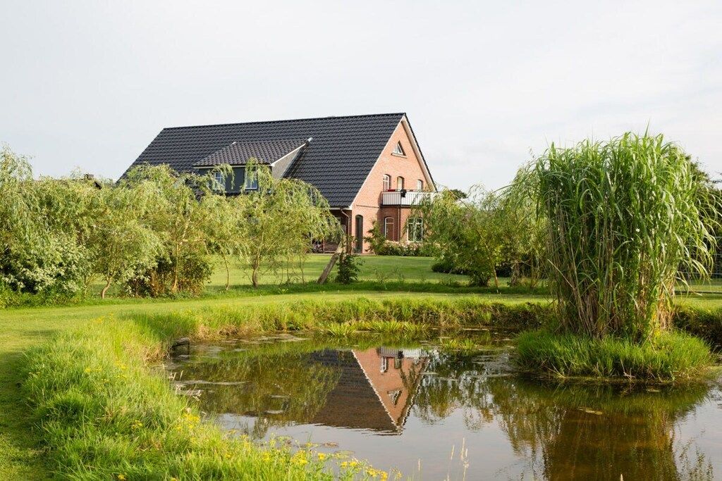 A house with a sloped roof, surrounded by a pond and greenery.
