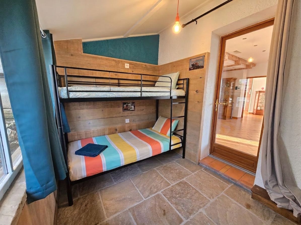 Habitación con literas, cabecera de madera, colcha a rayas de colores y suelo de baldosas de piedra.