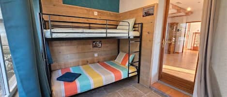 Habitación con literas, cabecera de madera, colcha a rayas de colores y suelo de baldosas de piedra.