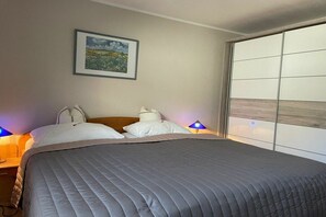 Ein Hotelzimmer mit Bett, zwei Nachttischlampen, einem gerahmten Bild an der Wand und einer Schiebetür rechts.