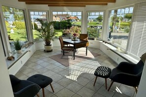 Una habitación iluminada por el sol con una mesa, sillas, ventanas amplias y vistas a un jardín.