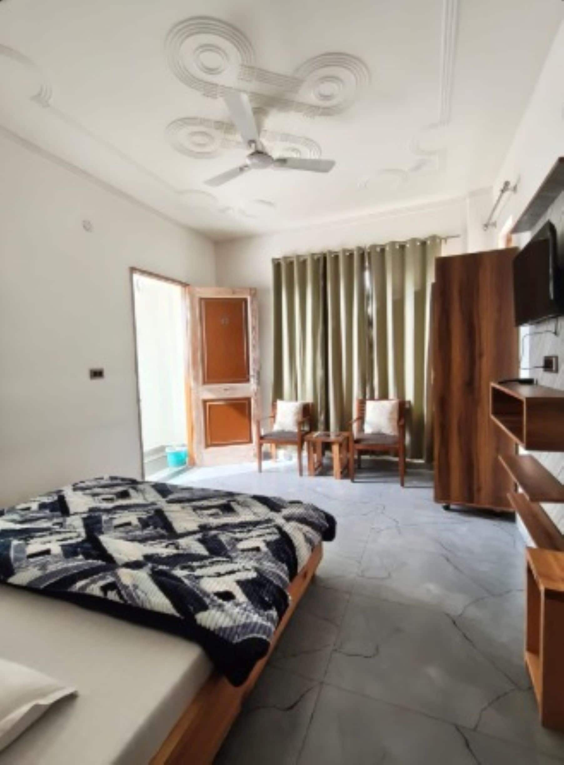 Una habitación de hotel con una cama, un ventilador de techo, un televisor y un armario de madera.