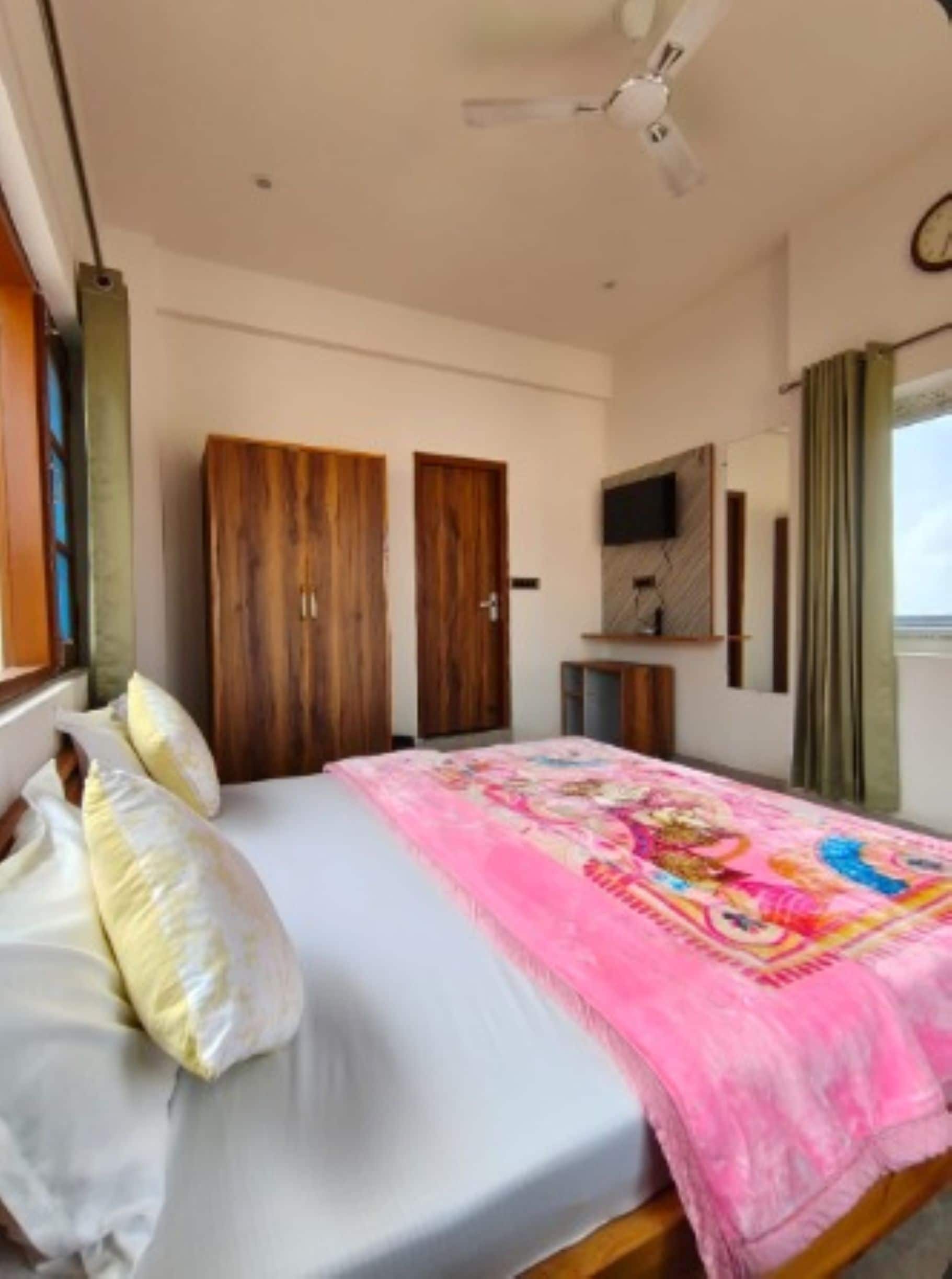 A bedroom with a bed, two wooden wardrobes, a television, and a window with curtains.