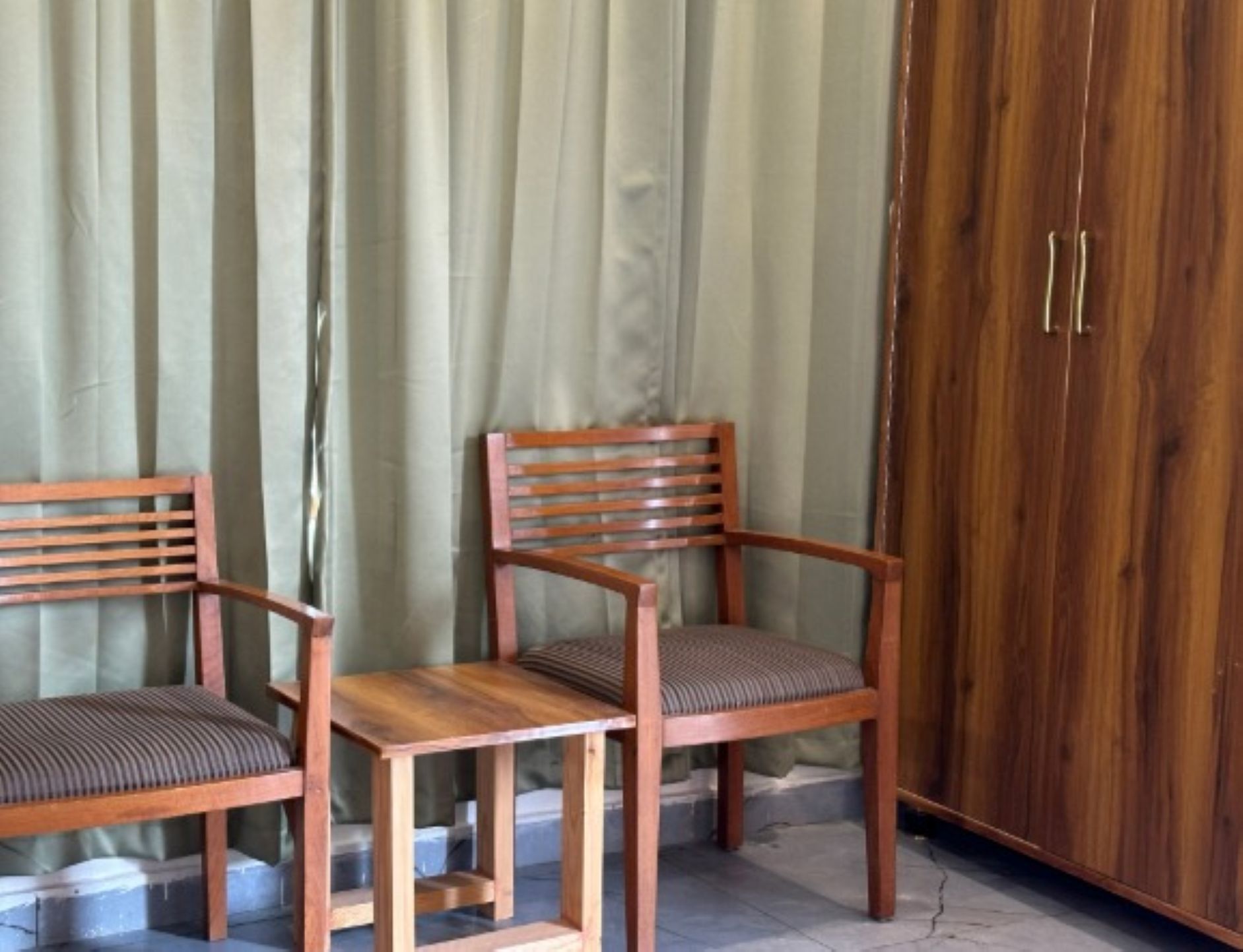 Two wooden chairs with cushioned seats and backs, positioned in front of a wooden wardrobe with two doors.