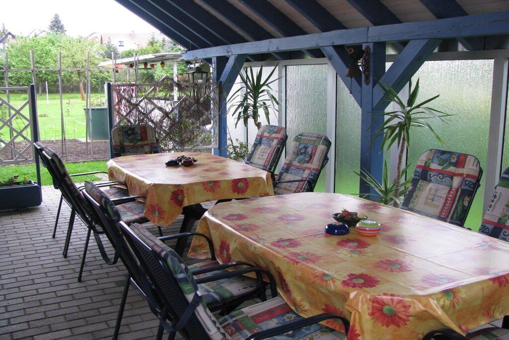 En udendørs patio med to borde dækket af blomstrede dug, omgivet af metalstole.