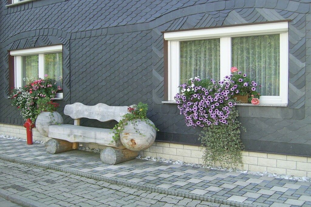A bench with potted plants beside a building with a patterned roof.