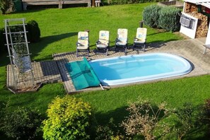 A swimming pool with a sunshade, surrounded by a grassy lawn and four lounge chairs. - Holiday apartment with 1 bedroom (Schleusingen OT Hinternah)
