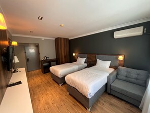 Habitación de hotel con dos camas, un escritorio, una silla, una lámpara y aire acondicionado instalado en la pared.