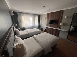 Habitación de hotel con dos camas, un televisor montado en la pared, una mesita y una ventana con cortinas.