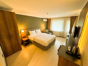 A hotel room with a bed, bedside tables, a desk with a coffee maker, a chair, a TV, and curtains. - GRAND PALACE HOTEL (Bartın)