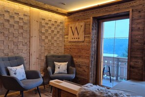 A room with two grey upholstered chairs, a wooden wall with a geometric pattern, and a large window with a view of a balcony.
