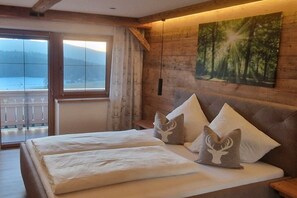 A bedroom with a bed, pillows, a painting, and a view of the outdoors.