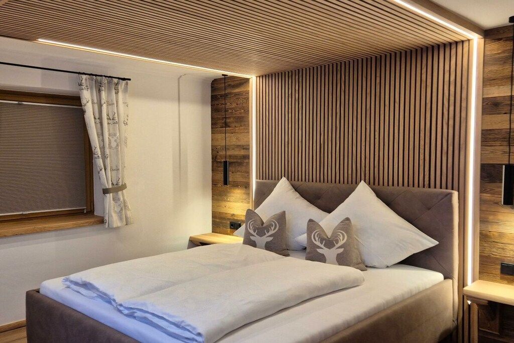 A modern bedroom with a wooden slatted headboard, a bed with white bedding, and a bedside table with a lamp.