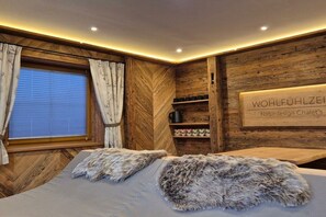 A room with a bed, wooden wall paneling, a window with curtains, and a shelf with items.