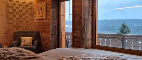 Una habitación con un ventanal grande, una pared de madera con diseño escocés y una cama con una manta de piel.