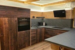 A compact kitchen with wooden cabinets, a built-in oven, a sink, and a black flat-screen TV mounted on the wall.