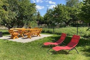 Ein Garten mit einem Holztisch und Bänken, umgeben von Gras und Bäumen.