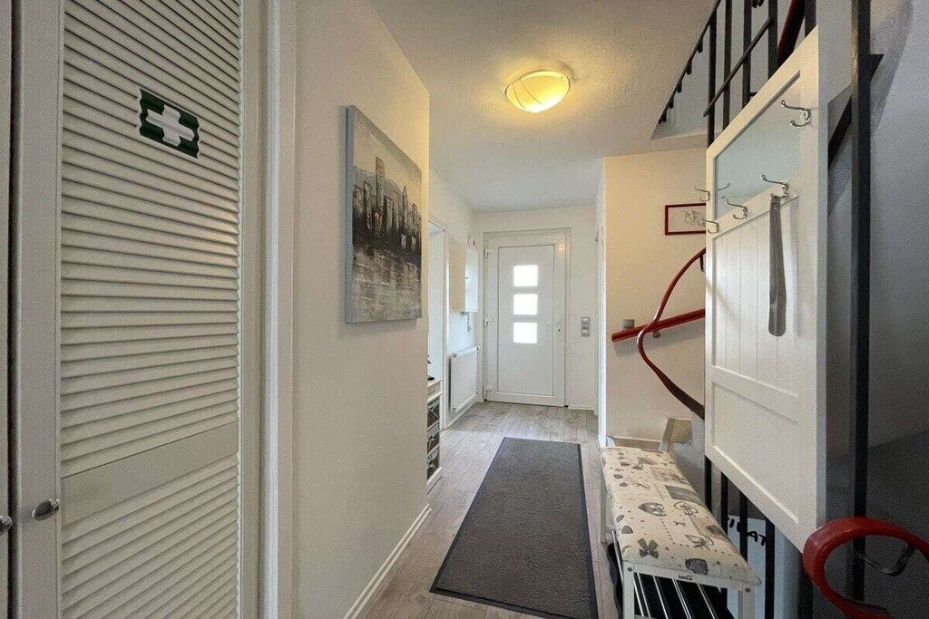 Un pasillo con una puerta, un perchero, un cuadro y una barandilla roja.