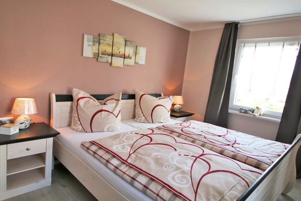 Une chambre à coucher avec un lit, des tables de chevet, une fenêtre avec des rideaux et des œuvres d’art murales.