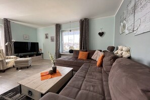 Ein Wohnzimmer mit einer Couch, einem Couchtisch, einem Fernseher und einem Fenster mit Vorhängen.