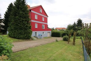 Ein rotes Gebäude mit einem grauen Unterteil, umgeben von einem gepflegten Rasen und einer hohen Nadelbaum-Hecke.