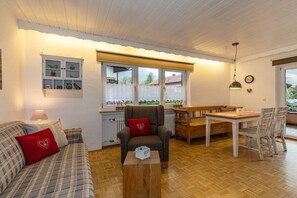 Ein gemütliches Wohnzimmer mit einer Couch, einem Sessel, einem Holztisch und einem Esstisch mit Stühlen.