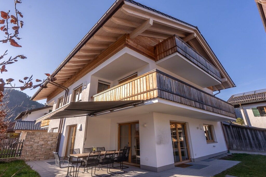 Une maison à deux étages dotée d’un balcon, d’une terrasse avec mobilier d’extérieur et offrant une vue sur les montagnes.
