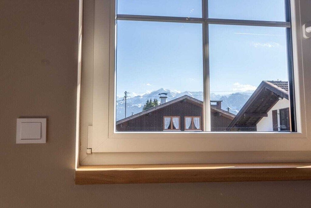 Une fenêtre donnant sur une montagne et un bâtiment doté d’un toit en pente.