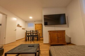 A compact living space with a flat-screen TV mounted on the wall, a wooden cabinet, a dining area with chairs, and a small table with a remote control. - Anuk House Holiday home with mountain views (Farchant)