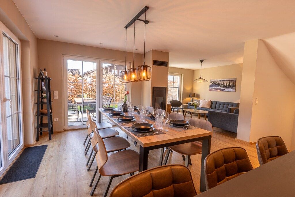 A dining area with a long table set for a meal, a sofa, and a fireplace in the background.