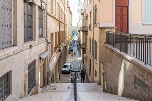 A narrow street with buildings on either side, a car parked on the street, and a person walking down the street. - L'Atelier - 2-Bedroom Apartment in Downtown (Lyon)