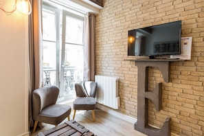 Ein modernes Wohnzimmer mit Backsteinwand, einem an der Wand befestigten Fernseher, zwei grauen Sesseln und einem Holztisch.