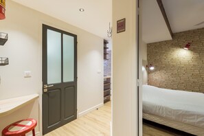 Una habitación con cama, piso de madera, pared de ladrillo y puerta con paneles de vidrio esmerilado.