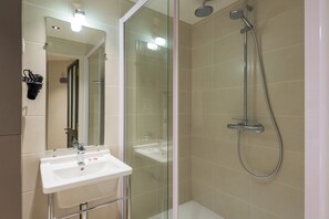 Ein modernes Badezimmer mit einer gläsernen Duschkabine, einem weißen Waschbecken und einem Spiegel.