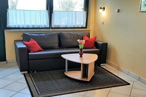 Ein Wohnzimmer mit einer Couch, einem kleinen Tisch und einer Blumenvase.