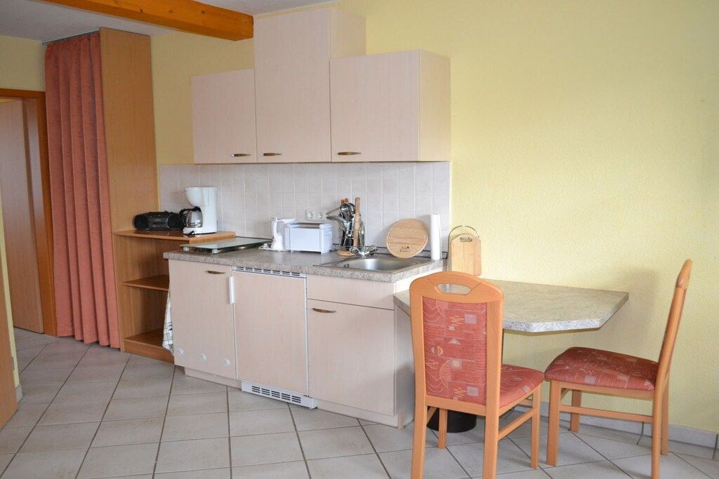 Cocina compacta con lavamanos, encimera y zona de comedor con dos sillas.