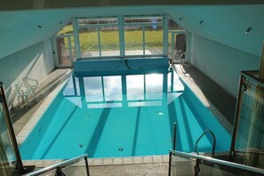 Ein Innenpool mit großen Glaswänden, gefliestem Boden und Blick ins Freie.