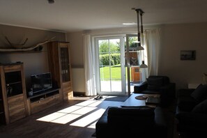Ein Wohnzimmer mit Fernseher, Sofa und einem großen Fenster mit Gartenblick.